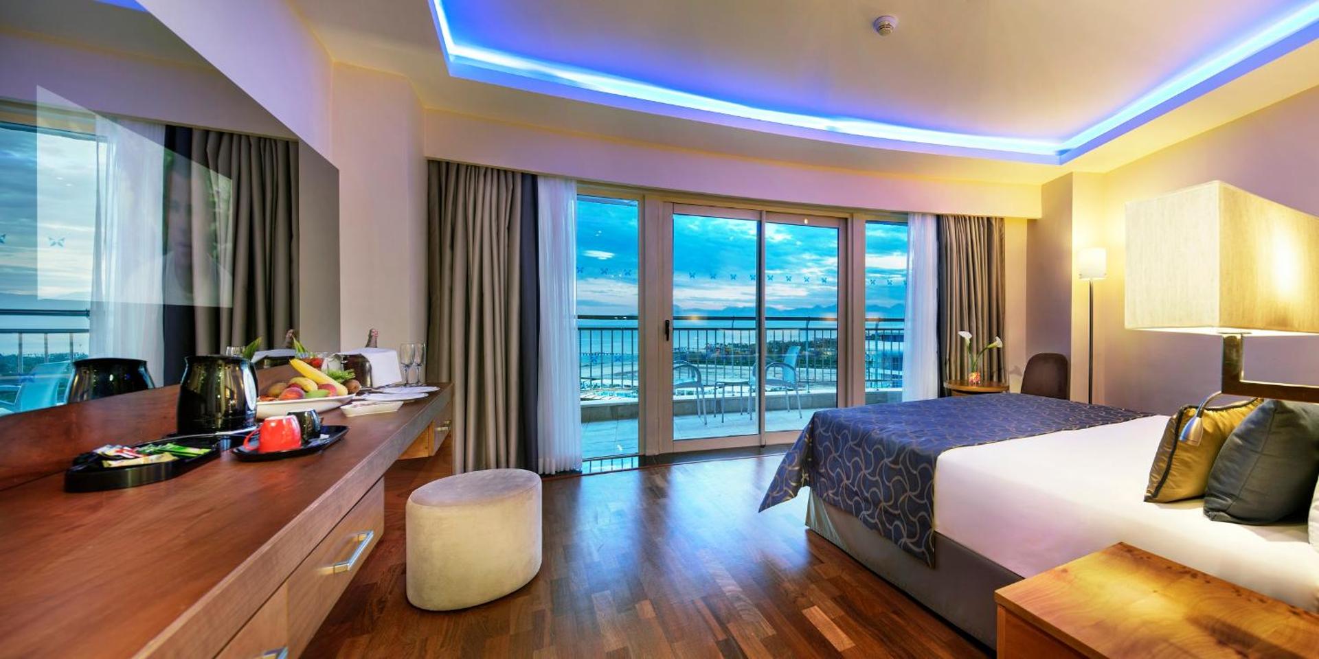 Liberty Hotels Lara moderns numurs ar skatu uz jūru, balkonu, koka grīdu un zilu griestu apgaismojumu Antaljas piekrastē