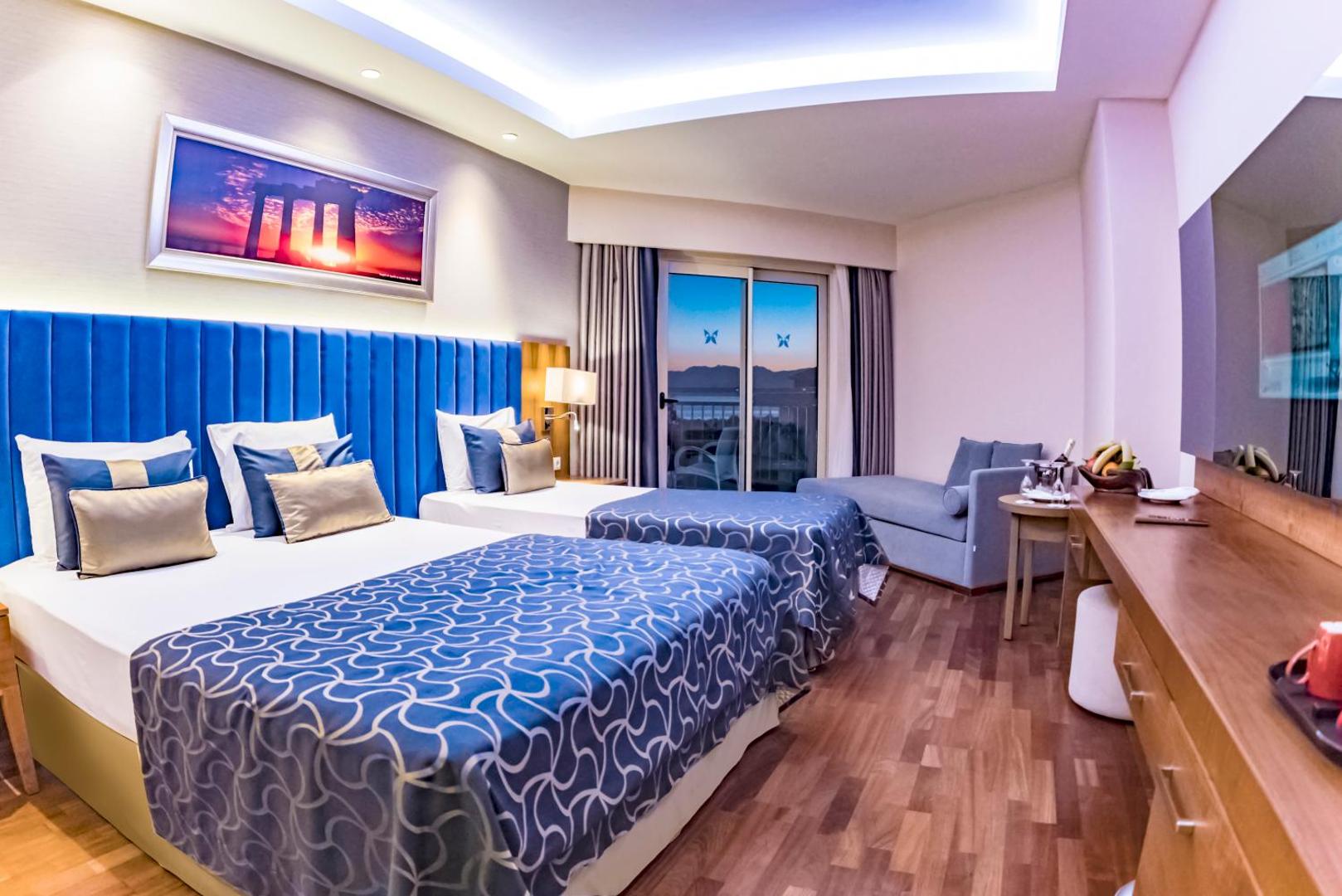 Liberty Hotels Lara plašs ģimenes numurs ar divām gultām, zilu galvgali un dīvānu atpūtas zonā Antaljā