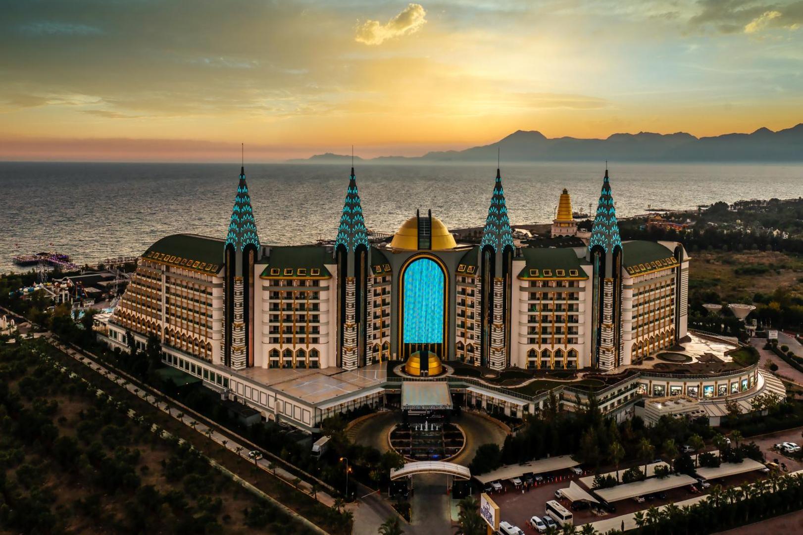 Delphin Imperial Hotel varenā ēka saulrietā Antaljā, Turcijā — skats no augšas uz arhitektūru, jūru un kalniem tālumā