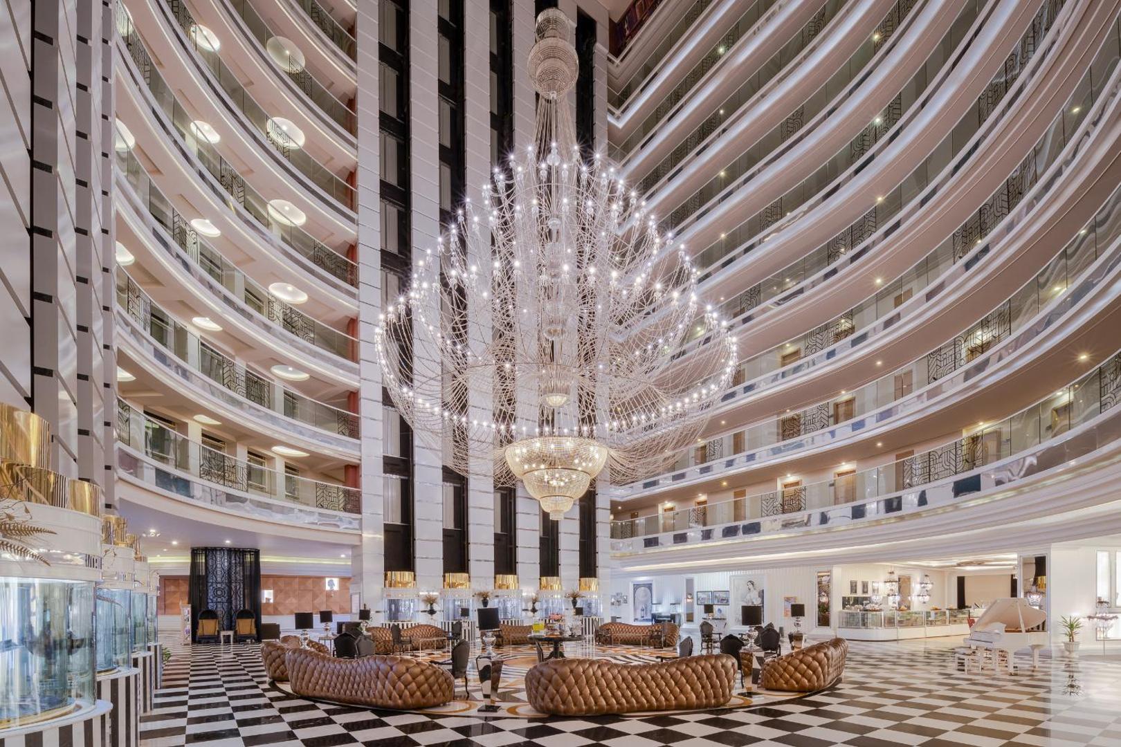 Delphin Imperial Hotel iespaidīgais ātrijs ar milzīgu kristāla lustru, vairākiem stāviem un mīkstajām mēbelēm centrā