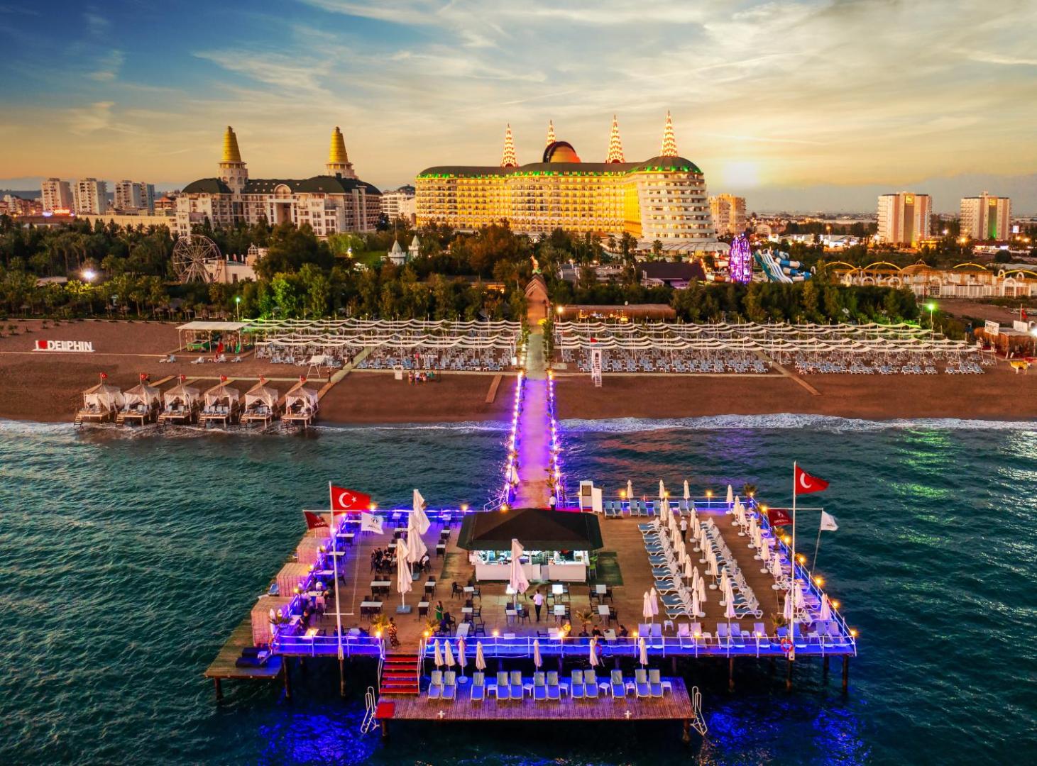 Delphin Imperial Hotel privātā pludmale un mols ar bāru vakarā — apgaismota atpūtas zona pie jūras Antaljas piekrastē