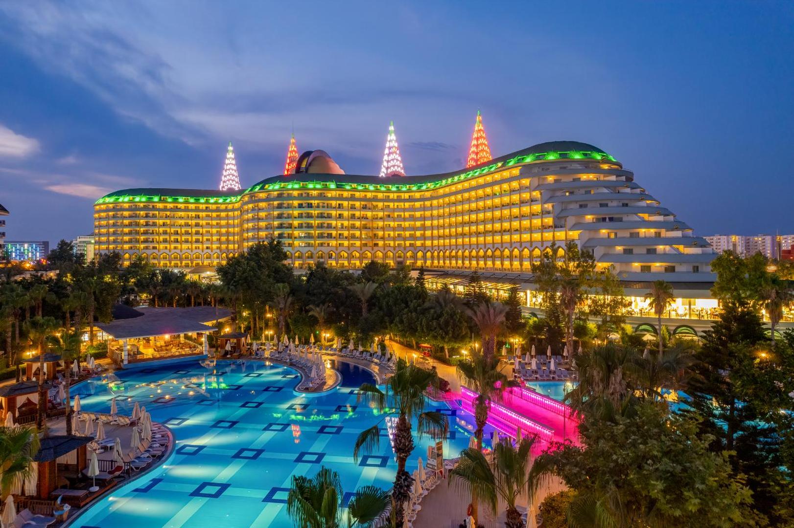 Delphin Imperial Hotel iespaidīgā arhitektūra vakarā ar izgaismotiem baseiniem un palmu dārzu Antaljā