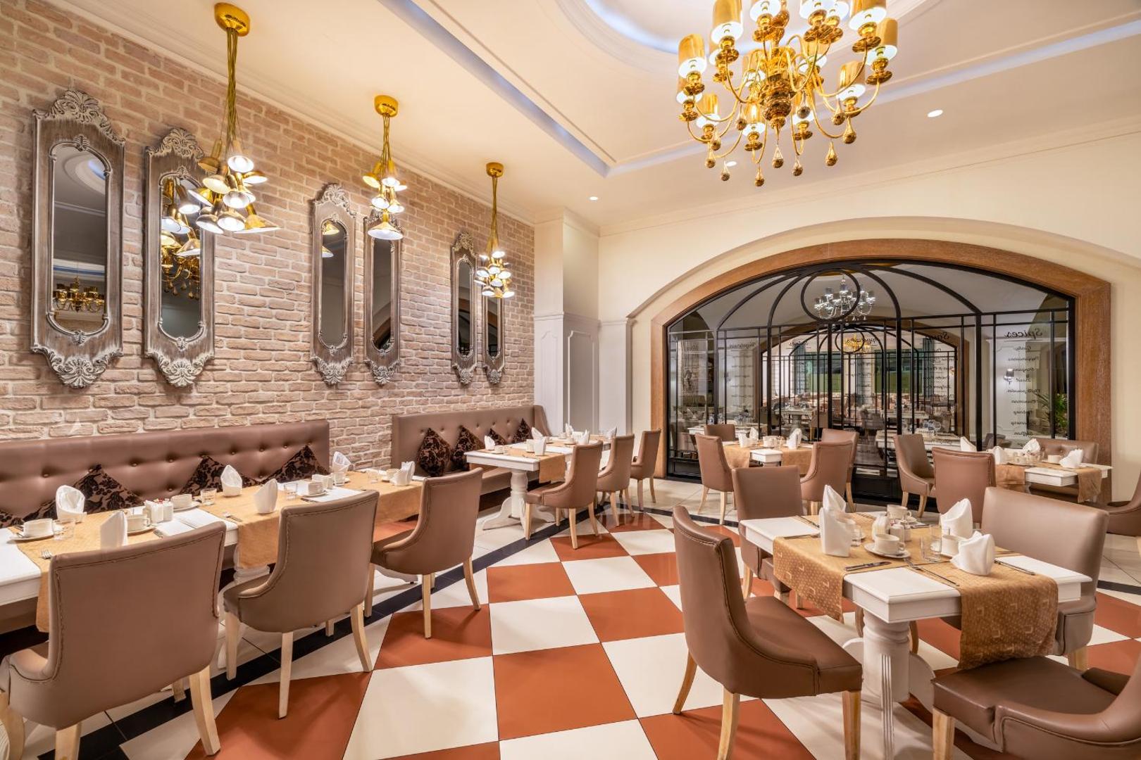 Delphin Imperial Hotel eleganta brokastu zāle ar klasisku interjeru — balti klāti galdi, dekoratīvi spoguļi un grezna lustra