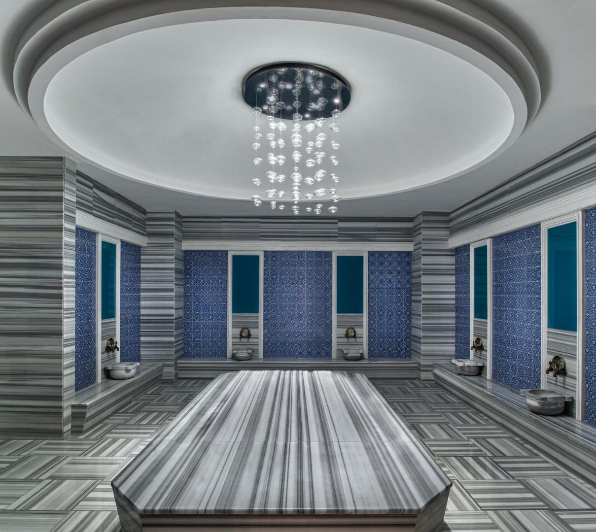 Aska Lara Resort & Spa tradicionālais turku hamams ar marmora apdari, ziliem flīžu dekoriem un centrālo masāžas galdu spa zonā