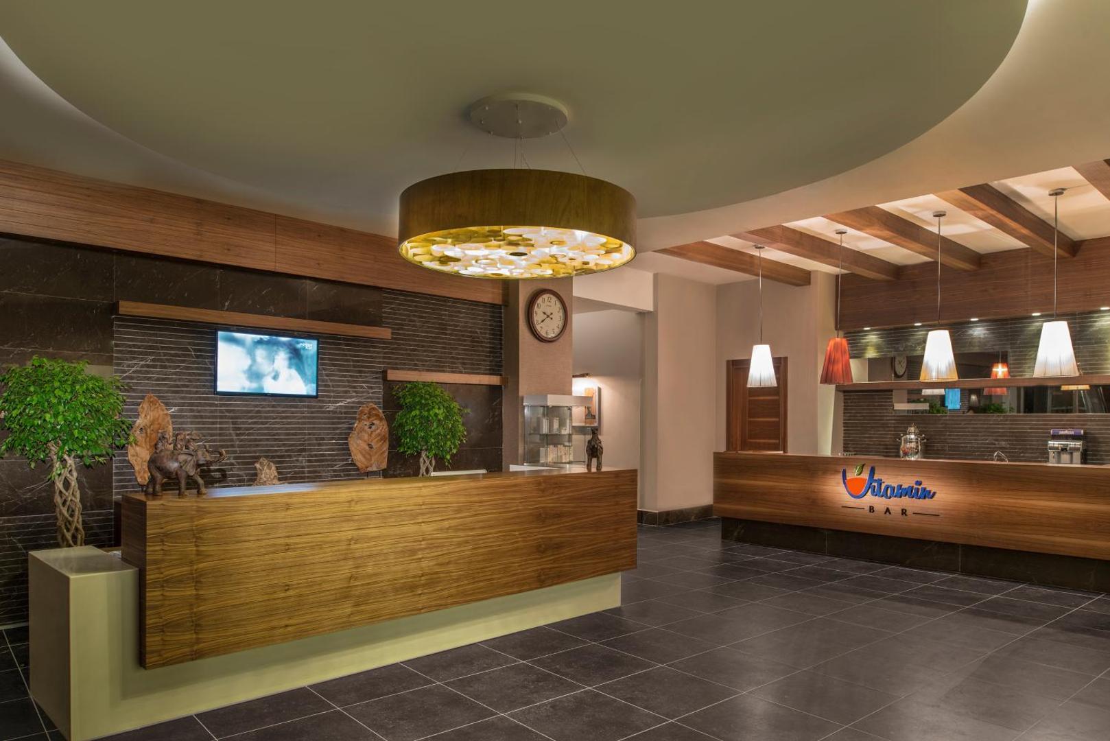 Aska Lara Resort & Spa viesnīcas lobby un Vitamin Bar zona ar koka apdari un modernu apgaismojumu Antālijā, Turcijā
