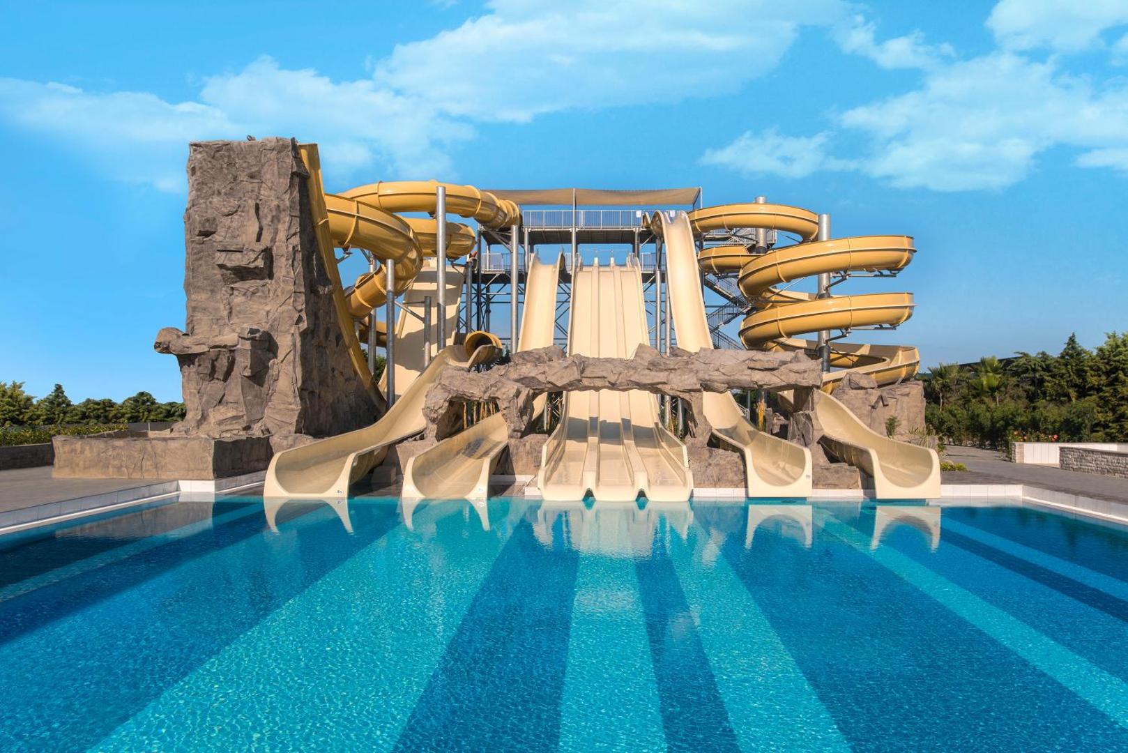 Aska Lara Resort & Spa akvaparka slidkalniņu komplekss pie dzidra baseina saulainā dienā Turcijā