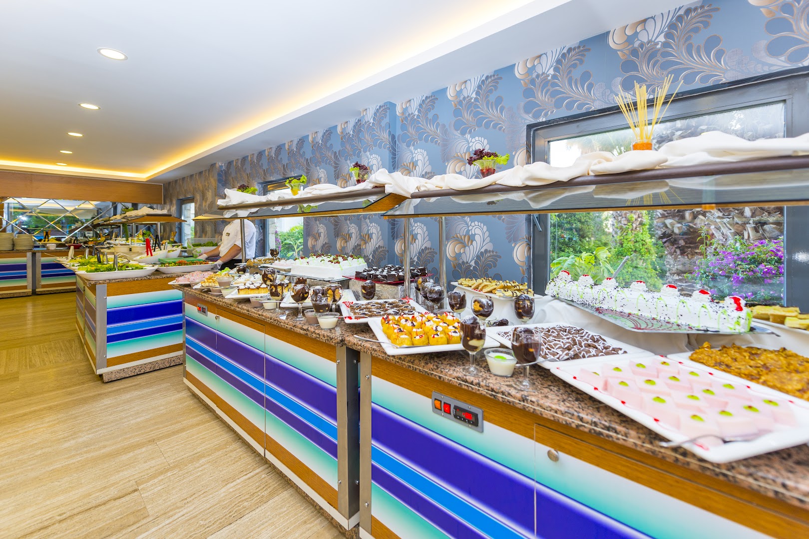 Club Aqua Plaza viesnīcas restorāna bufetes zona ar plašu desertu, kūku un uzkodu izvēli uz krāsainām servēšanas letēm.