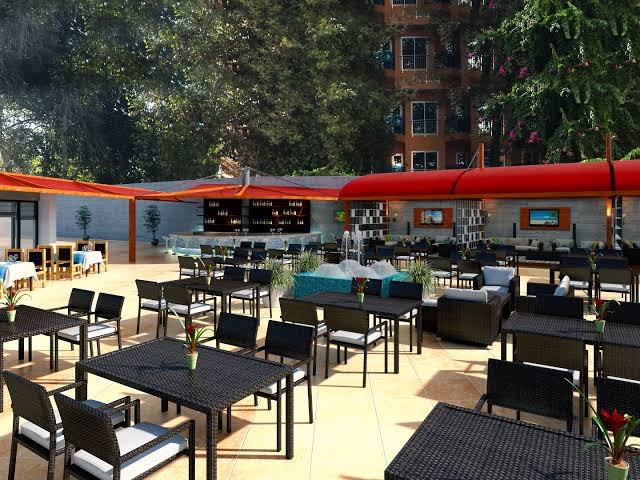 Club Aqua Plaza āra terases restorāns ar tumšām mēbelēm un sarkanām nojumēm Alānijas reģionā, Turcijā — plaša atpūtas zona pie viesnīcas