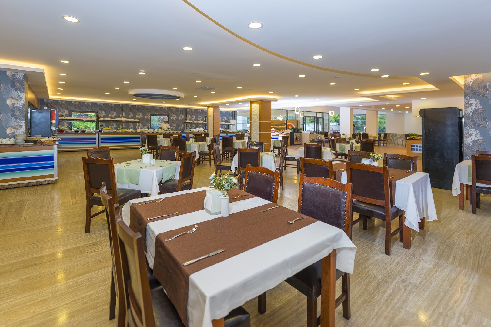 Club Aqua Plaza galvenais restorāns ar klātiem galdiem un bufetes zonu plašā, gaišā telpā ar modernu apgaismojumu