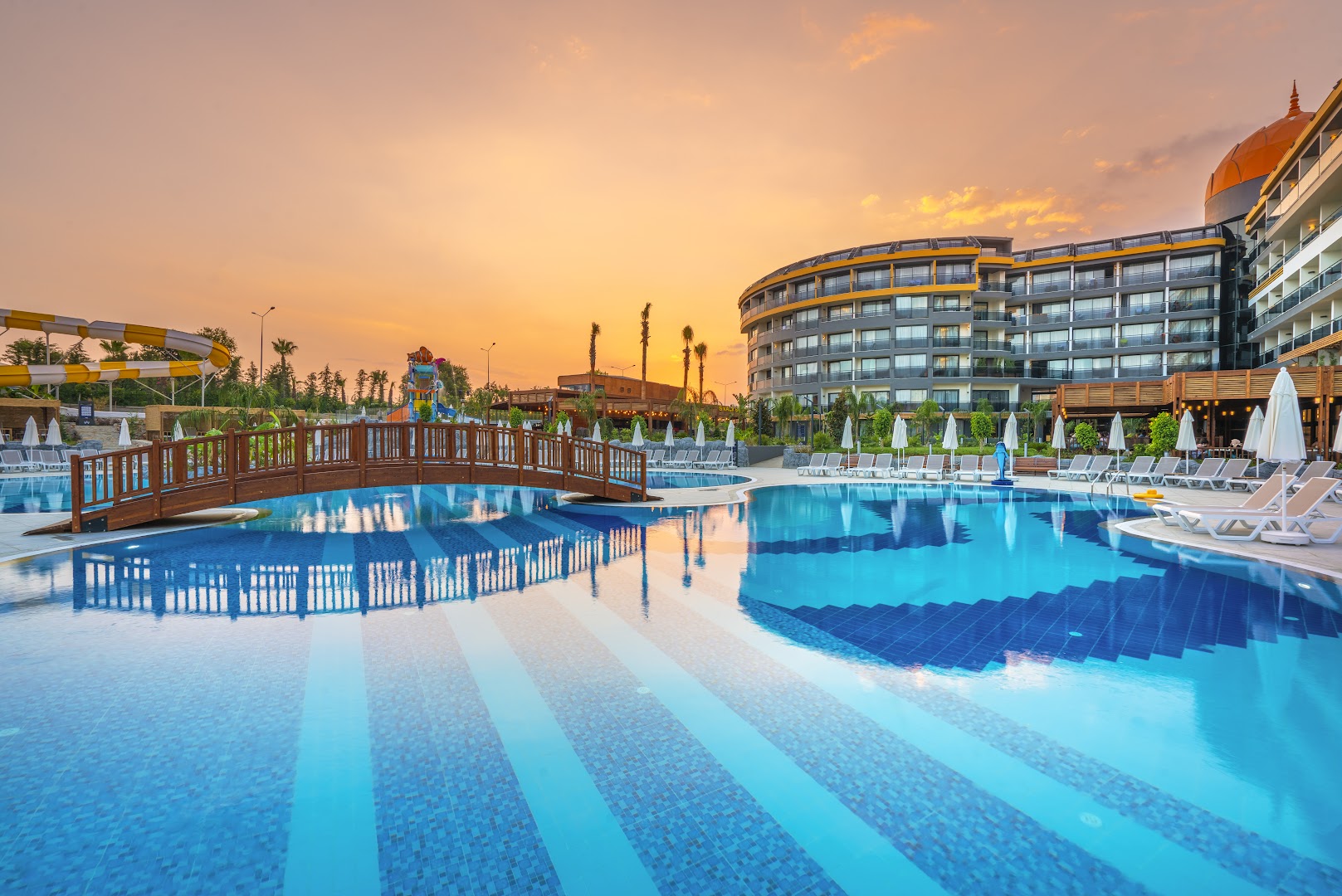 Arnor De Luxe Hotel & Spa baseina zona ar koka tiltiņu un sauļošanās krēsliem zelta stundā Turcijas piekrastē