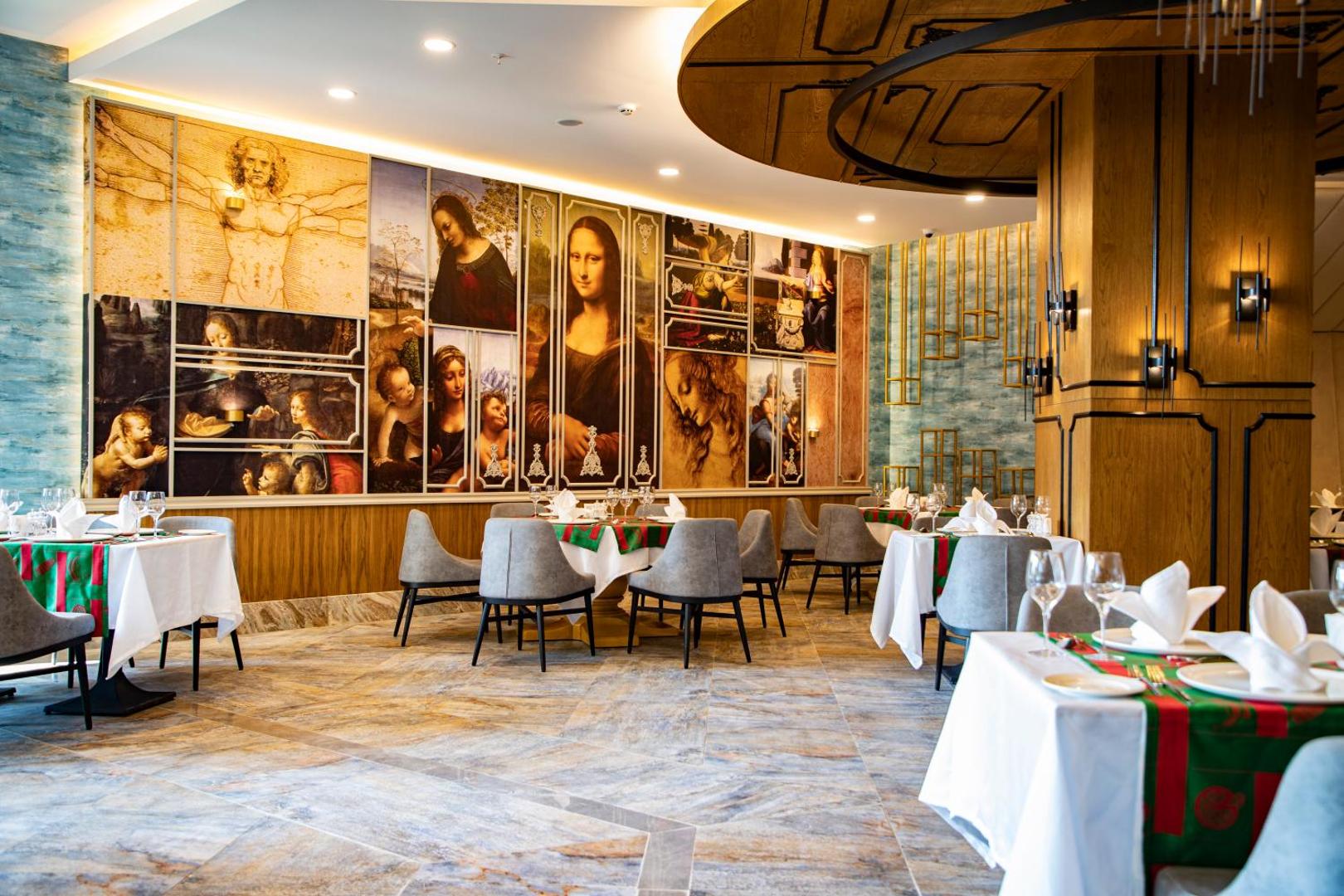 Arnor De Luxe Hotel & Spa tematiskais restorāns ar mākslas reprodukcijām pie sienām, eleganti klātiem galdiem un greznu interjeru.