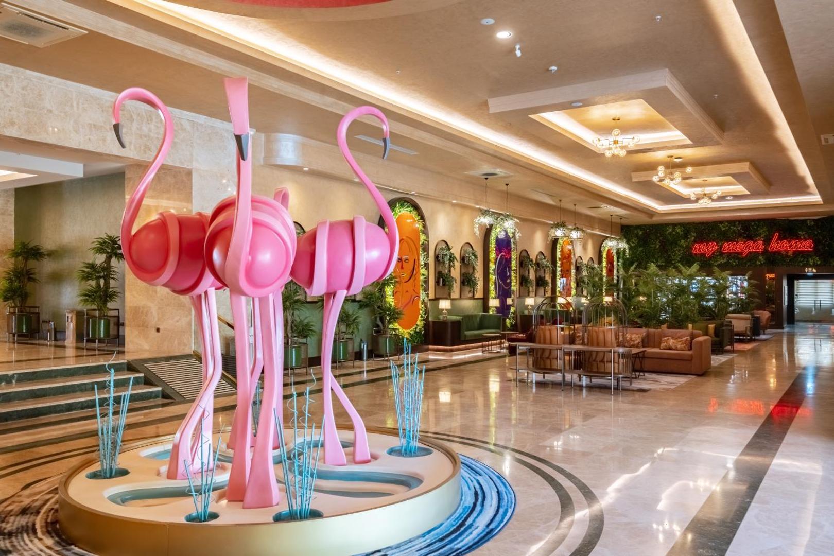 Megasaray Westbeach Antalya viesnīcas vestibils ar rozā flamingo skulptūrām, modernām mēbelēm un plašu atpūtas zonu Antaljas piekrastē, Turcijā