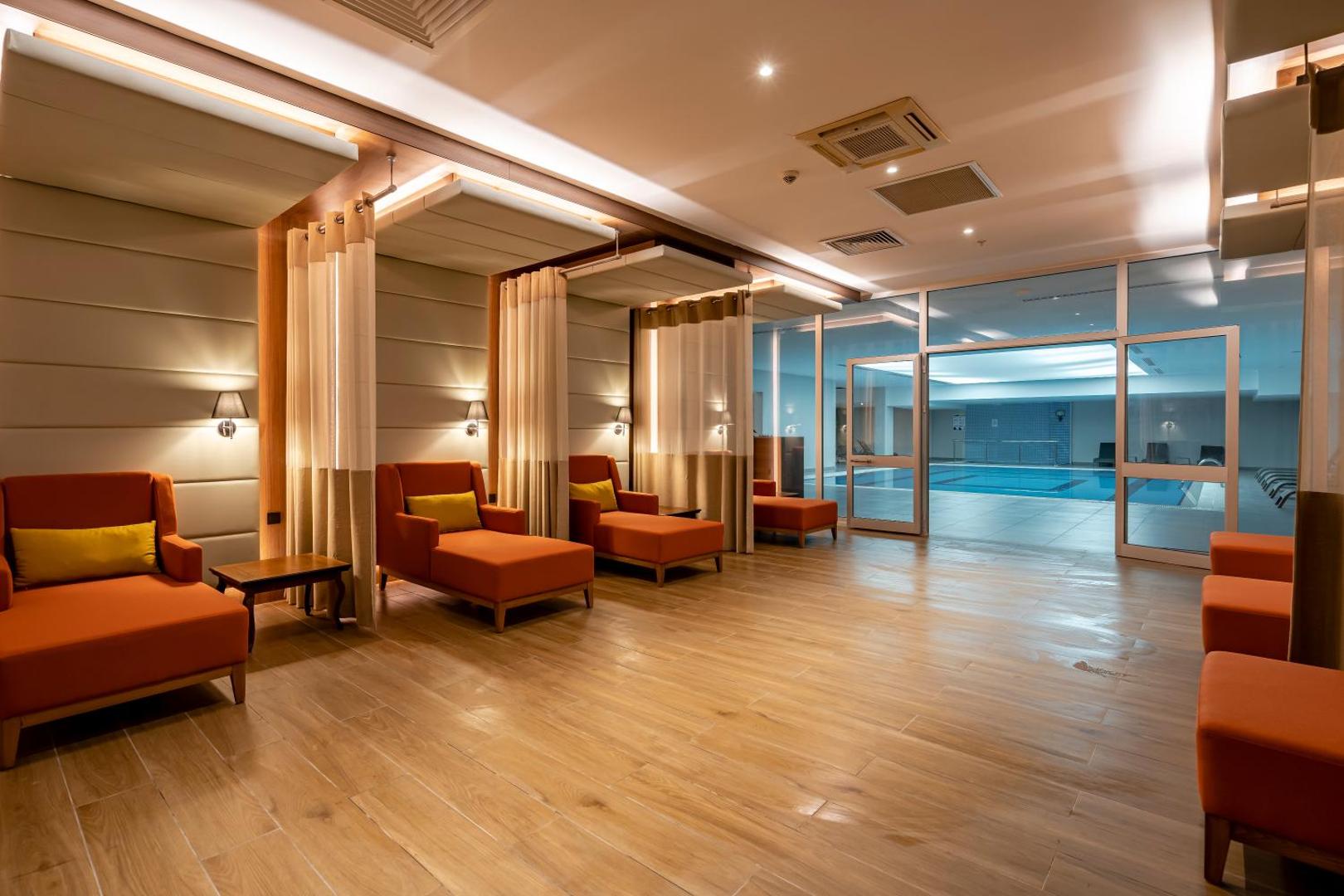 Megasaray Westbeach Antalya spa zonas atpūtas telpa ar oranžiem zviļņiem un skatu uz iekštelpu baseinu caur stikla sienu