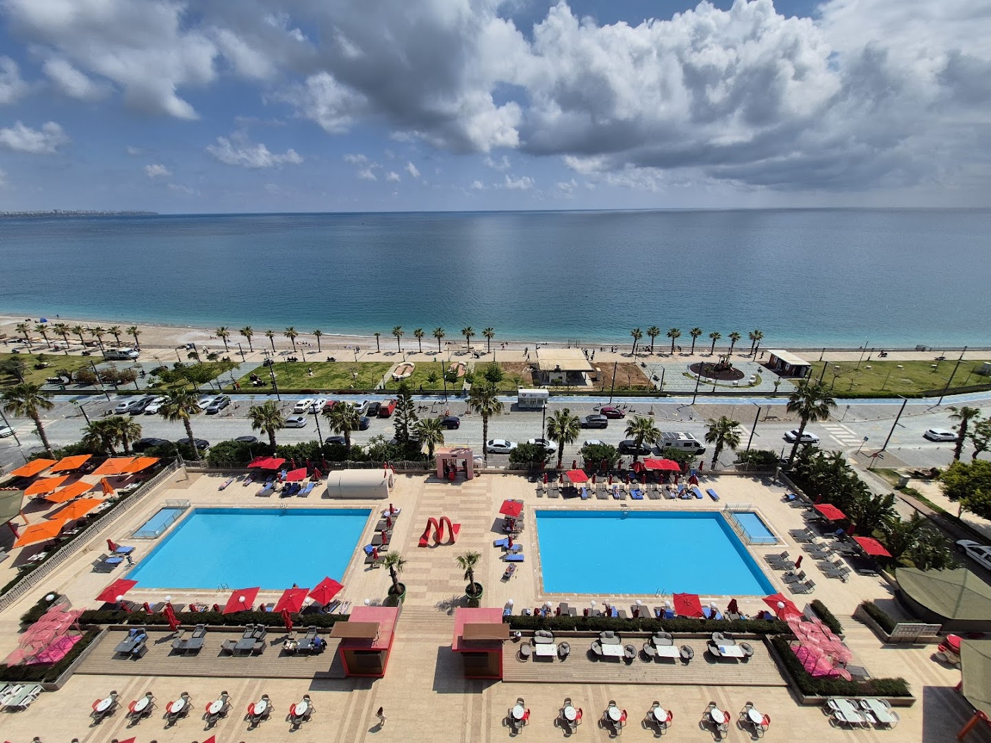 Megasaray Westbeach Antalya skats no augšas uz diviem āra baseiniem, atpūtas zonu ar saulessargiem un Vidusjūras piekrasti Antaljā
