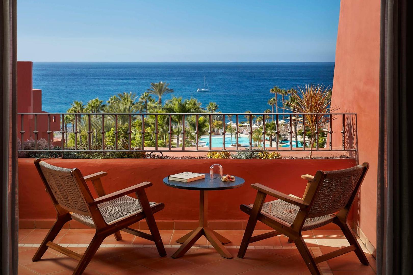Skats no Tivoli La Caleta Tenerife Resort numura balkona uz zilo okeānu, palmām un viesnīcas baseinu zonu
