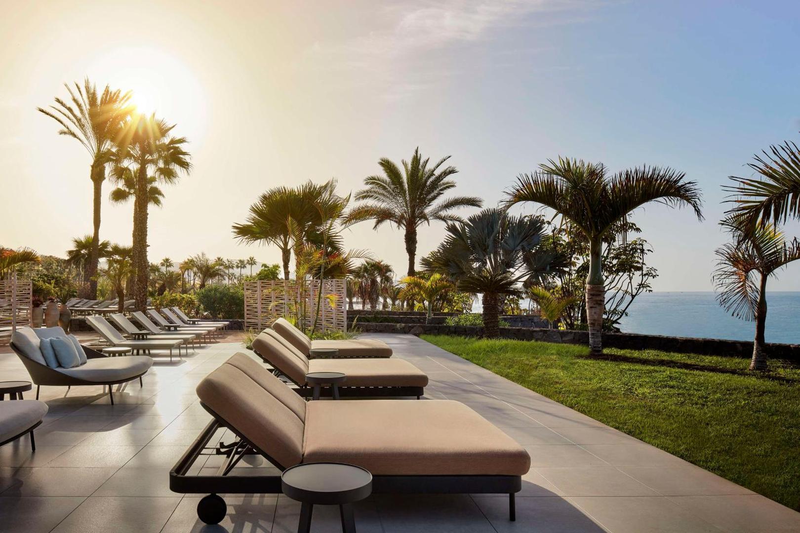 Tivoli La Caleta Tenerife Resort sauļošanās zona ar mīkstiem zviļņiem, zaļu zālienu un palmām okeāna piekrastē