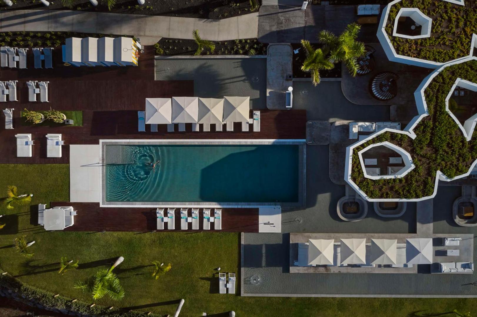 Royal Hideaway Corales Beach viesnīcas teritorijas skats no augšas — baseins, sauļošanās zona ar lietussargiem un modernu arhitektūru Tenerifē