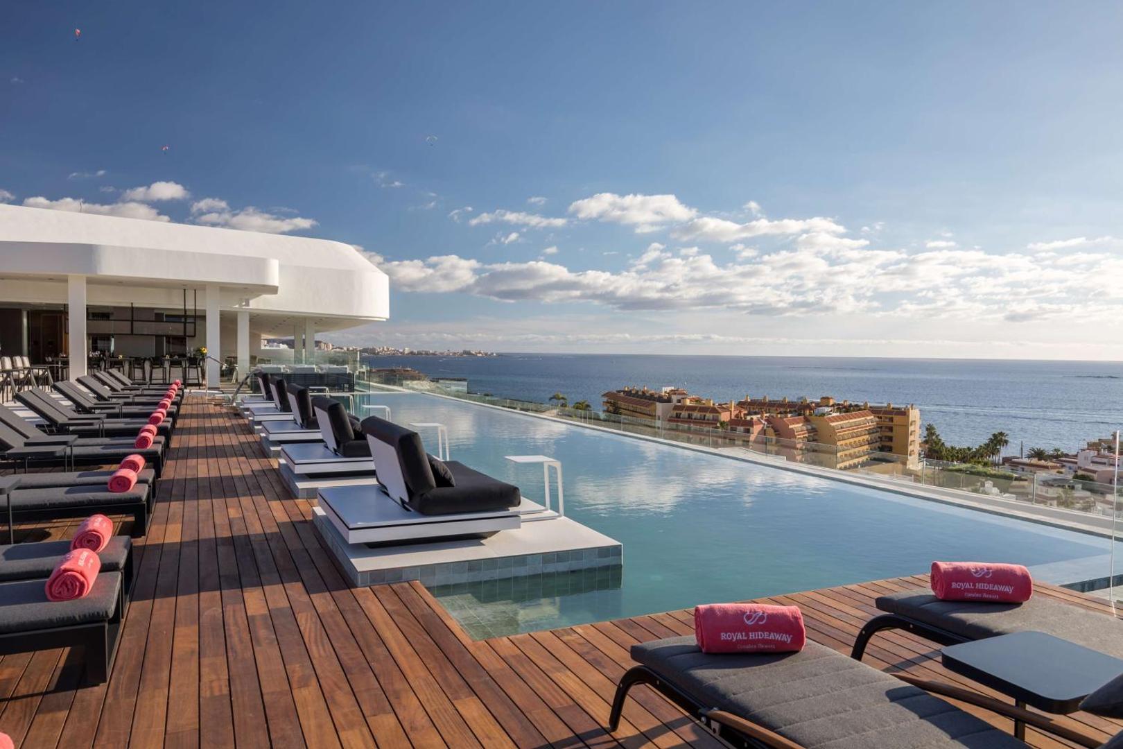 Royal Hideaway Corales Beach baseins ar pārplūdes malu un skatu uz okeānu — koka terase ar atpūtas krēsliem Tenerifes piekrastē
