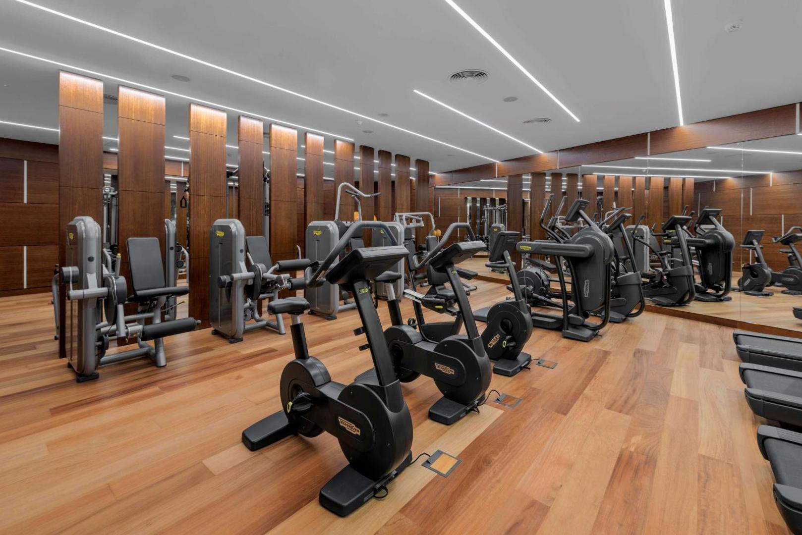 Royal Hideaway Corales Beach moderns fitness centrs ar Technogym aprīkojumu un koka apdari — plaša trenažieru zāle viesu labsajūtai