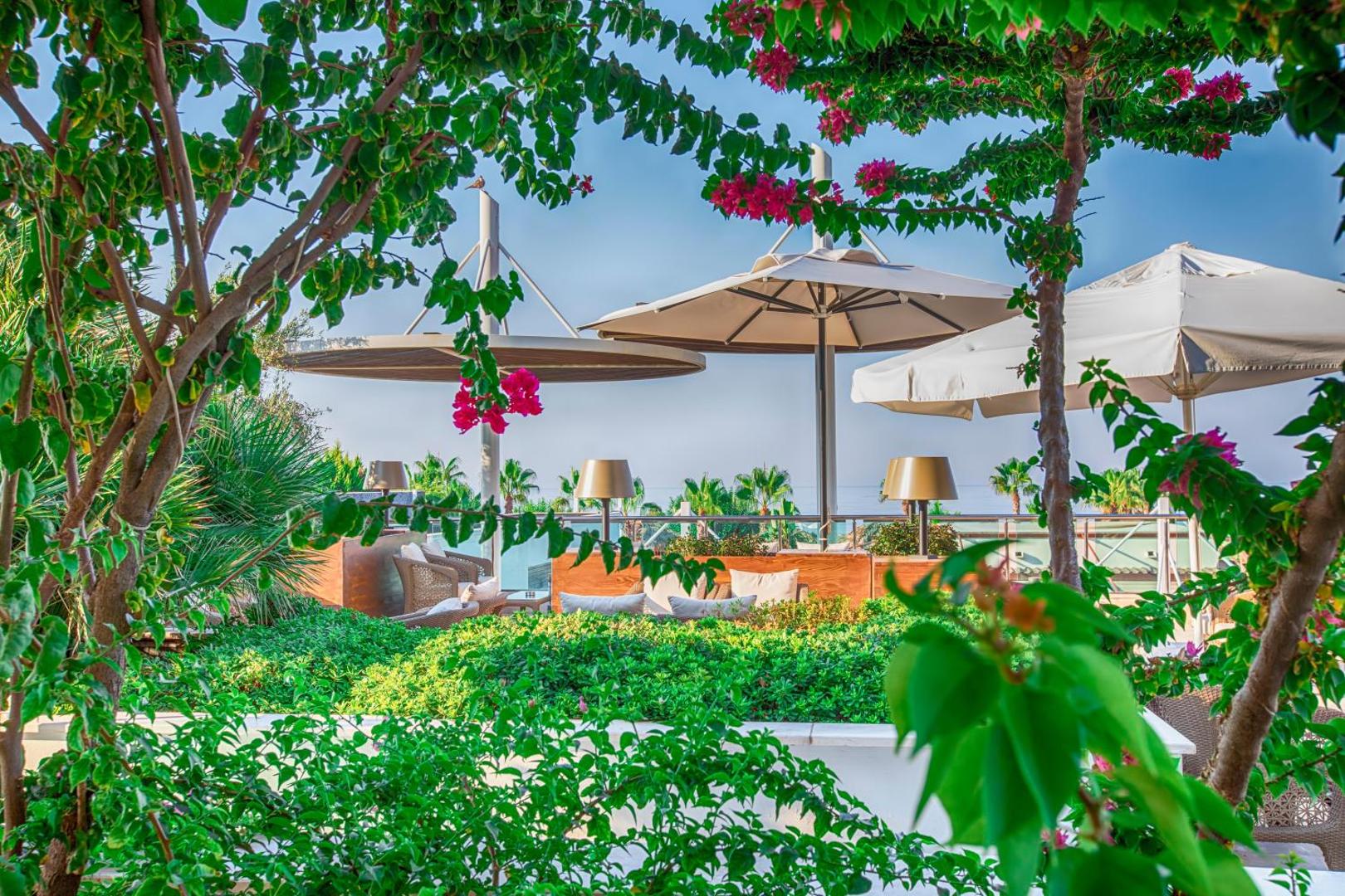 Sherwood Blue Belek viesnīcas jumta terase ar ziedošiem krūmiem, saulessargiem un skatu uz jūru Belekas kūrortā