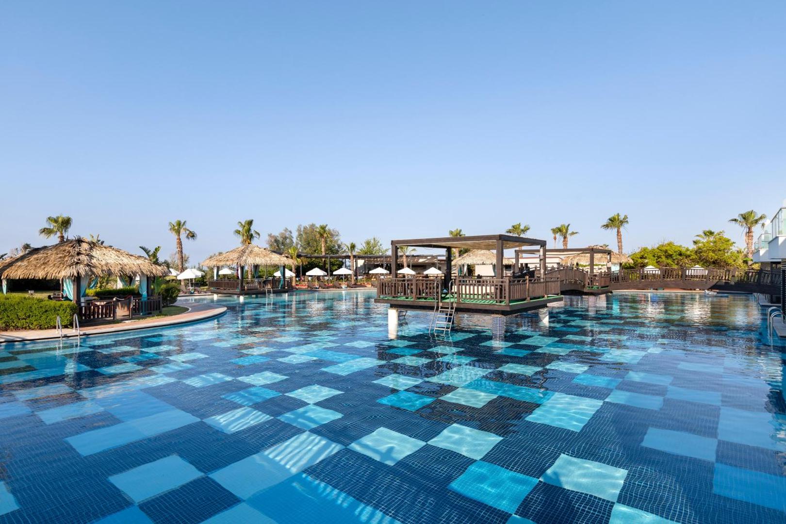 Sherwood Blue Belek plašais āra baseins ar ziliem flīžu rakstiem, atpūtas nojumēm un palmām Belekas reģionā, Turcijā