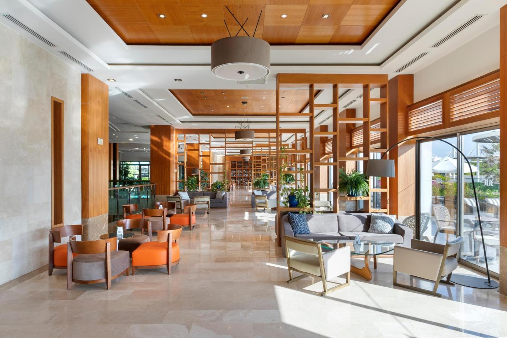 Sherwood Blue Belek plašā lobby zona ar modernām mēbelēm, koka dizaina elementiem un lieliem logiem