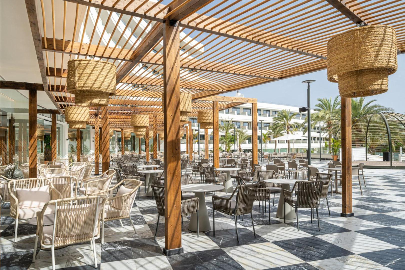 Mediterranean Palace viesnīcas āra terase ar modernām mēbelēm un koka pergolu Tenerifē — plaša atpūtas zona ar pītiem gaismekļiem