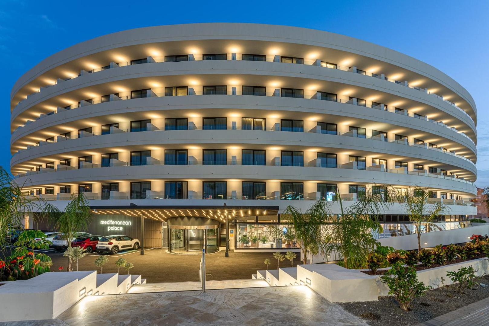 Viesnīcas Mediterranean Palace modernā fasāde vakarā ar izgaismotiem balkoniem un galveno ieeju Tenerifē, arhitektūras detaļas nakts apgaismojumā