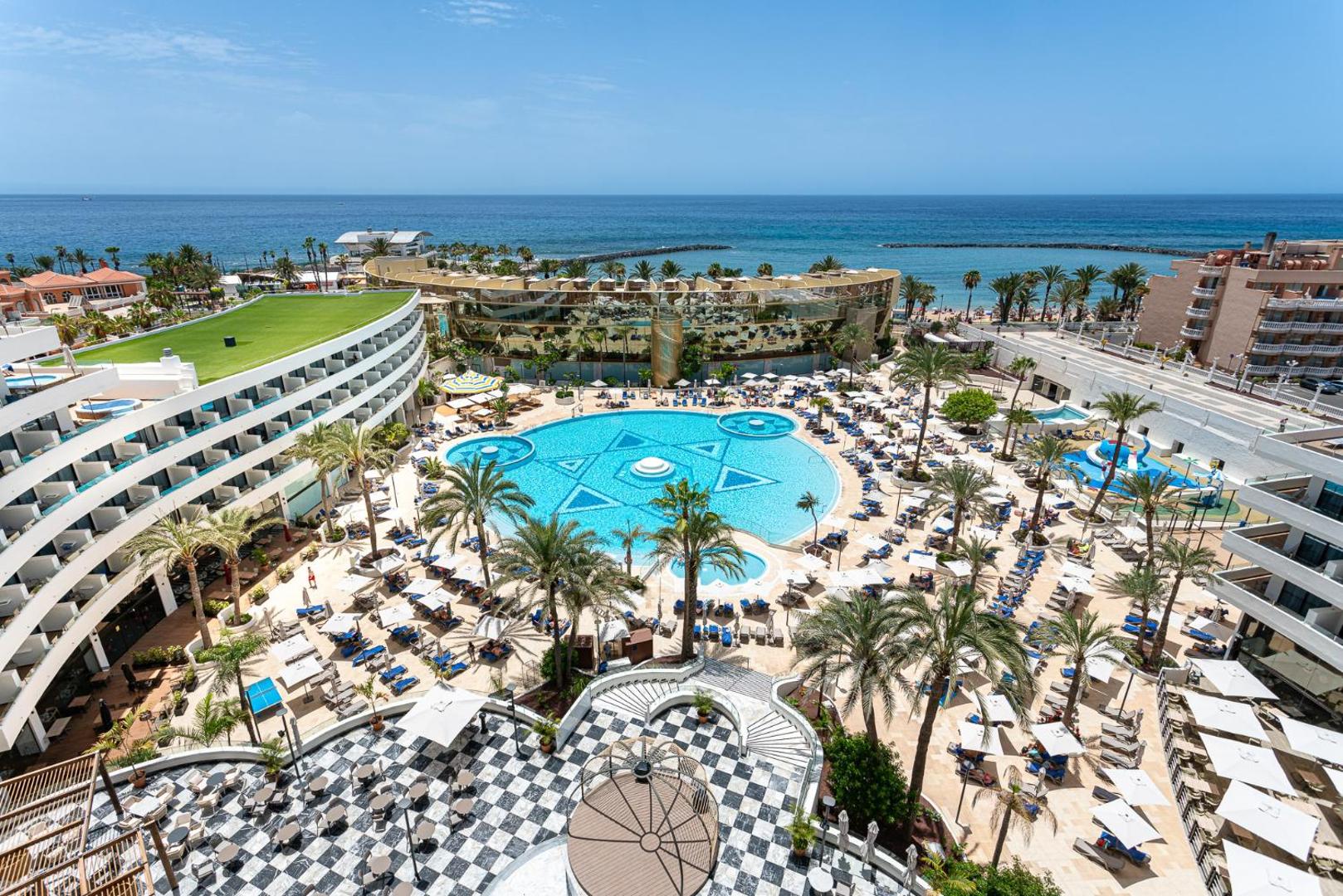 Mediterranean Palace viesnīcas plašais āra baseins ar palmu ieskautu atpūtas zonu Tenerifes piekrastē, skats uz okeānu un saulainu terasi
