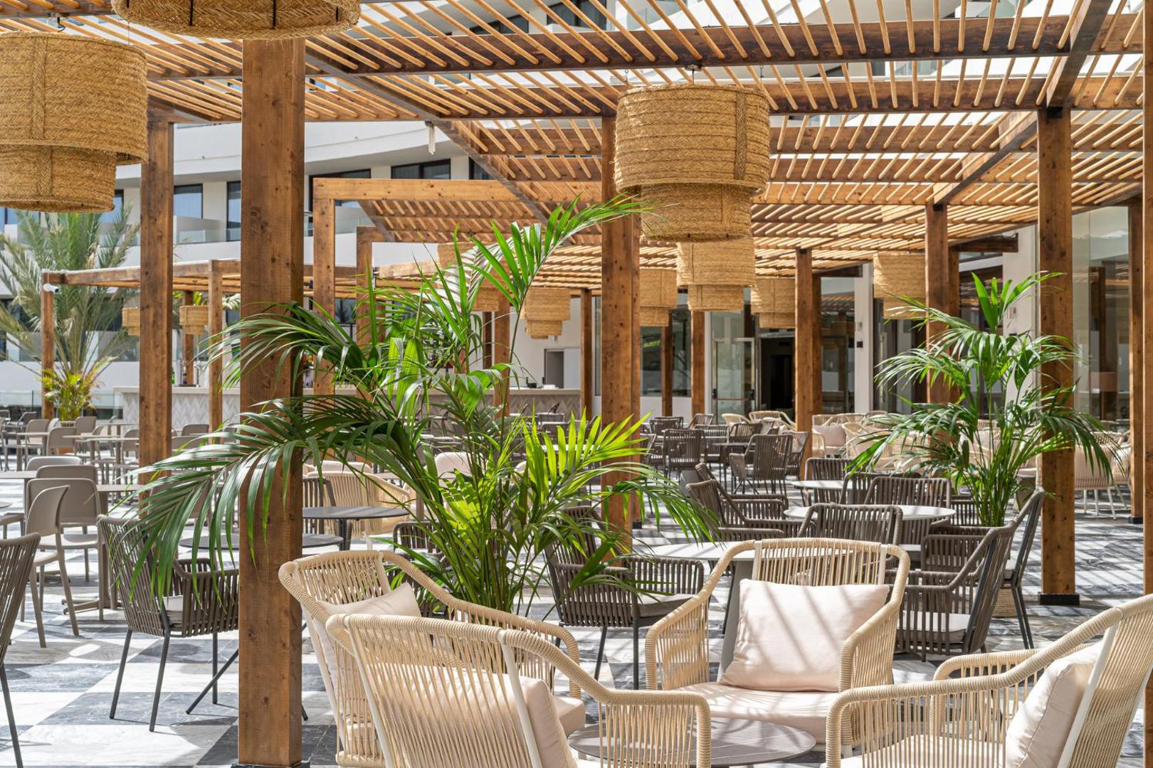 Mediterranean Palace viesnīcas terases fragments ar palmām un pītiem krēsliem koka nojumes ēnā — atpūtas zona kūrortā Tenerifē