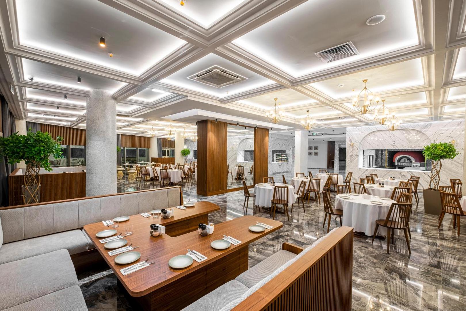 Plašs Rubi Platinum Sign galvenais restorāns ar marmora grīdām, baltiem galdautiem un atvērto virtuvi fonā
