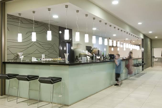 Kn Columbus Aparthotel modernais vestibila bārs ar gaišu leti, augstiem krēsliem un stilīgu apgaismojumu viesnīcas iekštelpās Tenerifē.