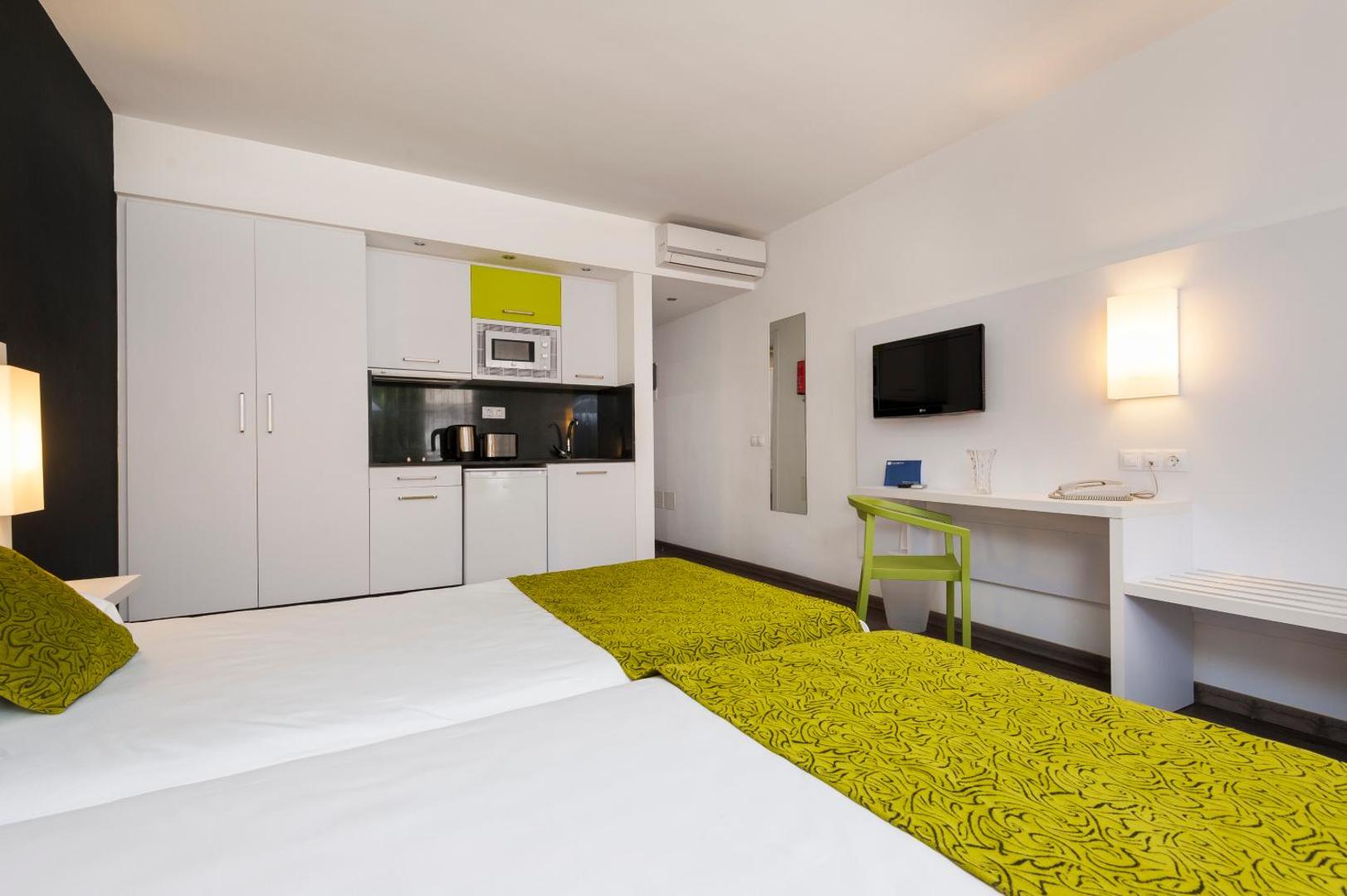 Kn Columbus Aparthotel studijas tipa numurs ar virtuves zonu un divām gultām Tenerifē — gaišs interjers ar zaļiem akcentiem