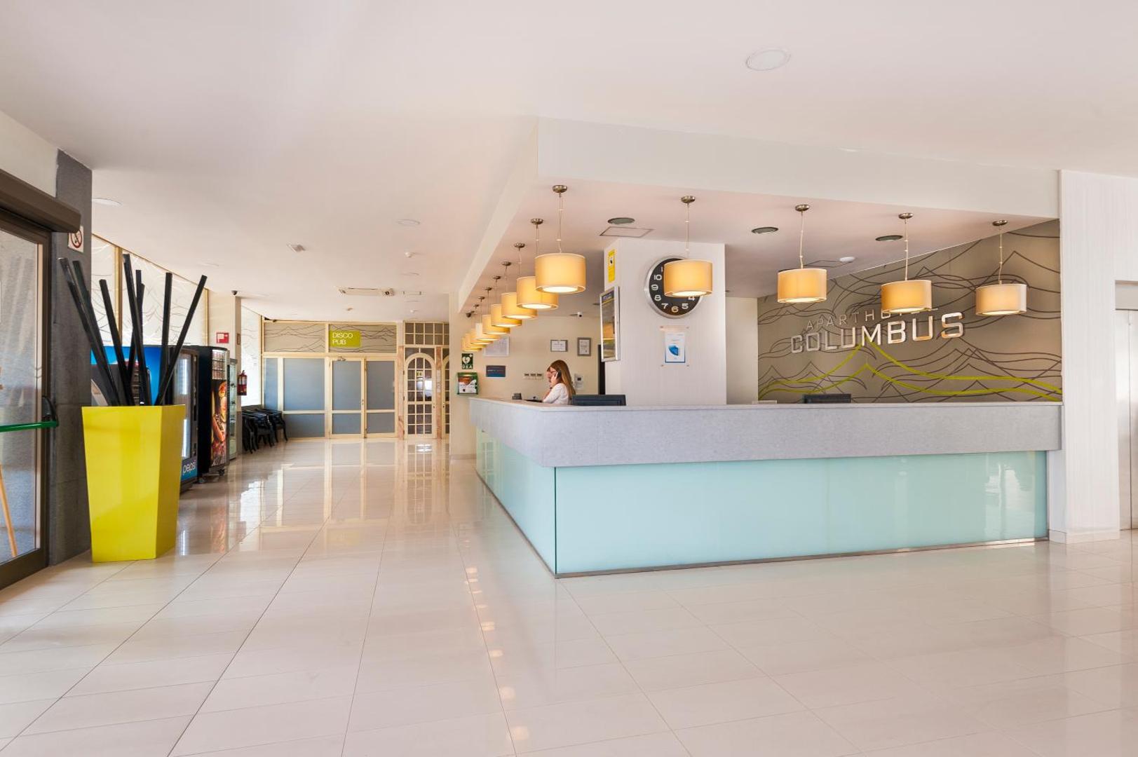 Kn Columbus Aparthotel gaišā recepcijas zona Tenerifē ar modernu leti, siltu apgaismojumu un viesmīlīgu personālu tūristu uzņemšanai