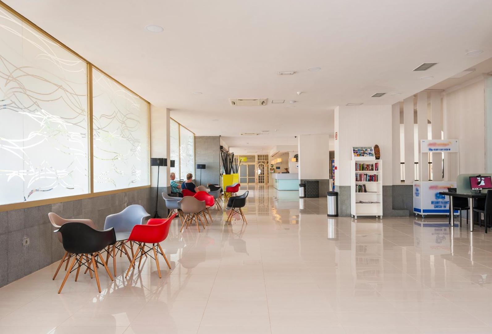 Kn Columbus Aparthotel plašais vestibils ar krāsainiem atpūtas krēsliem, informācijas stendu un gaišu interjeru Tenerifes dienvidos