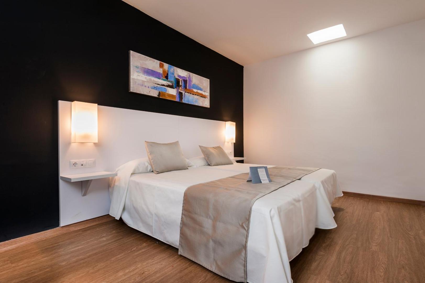 Kn Columbus Aparthotel moderns numurs ar tumšu akcenta sienu un divām gultām — minimālisma stils un silts apgaismojums