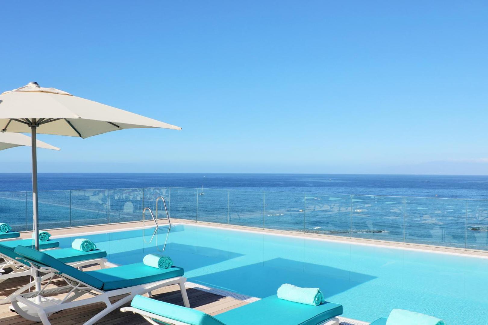Iberostar Sabila bezmalas baseins uz jumta terases ar tirkīza sauļošanās krēsliem un skatu uz Atlantijas okeānu Tenerifē