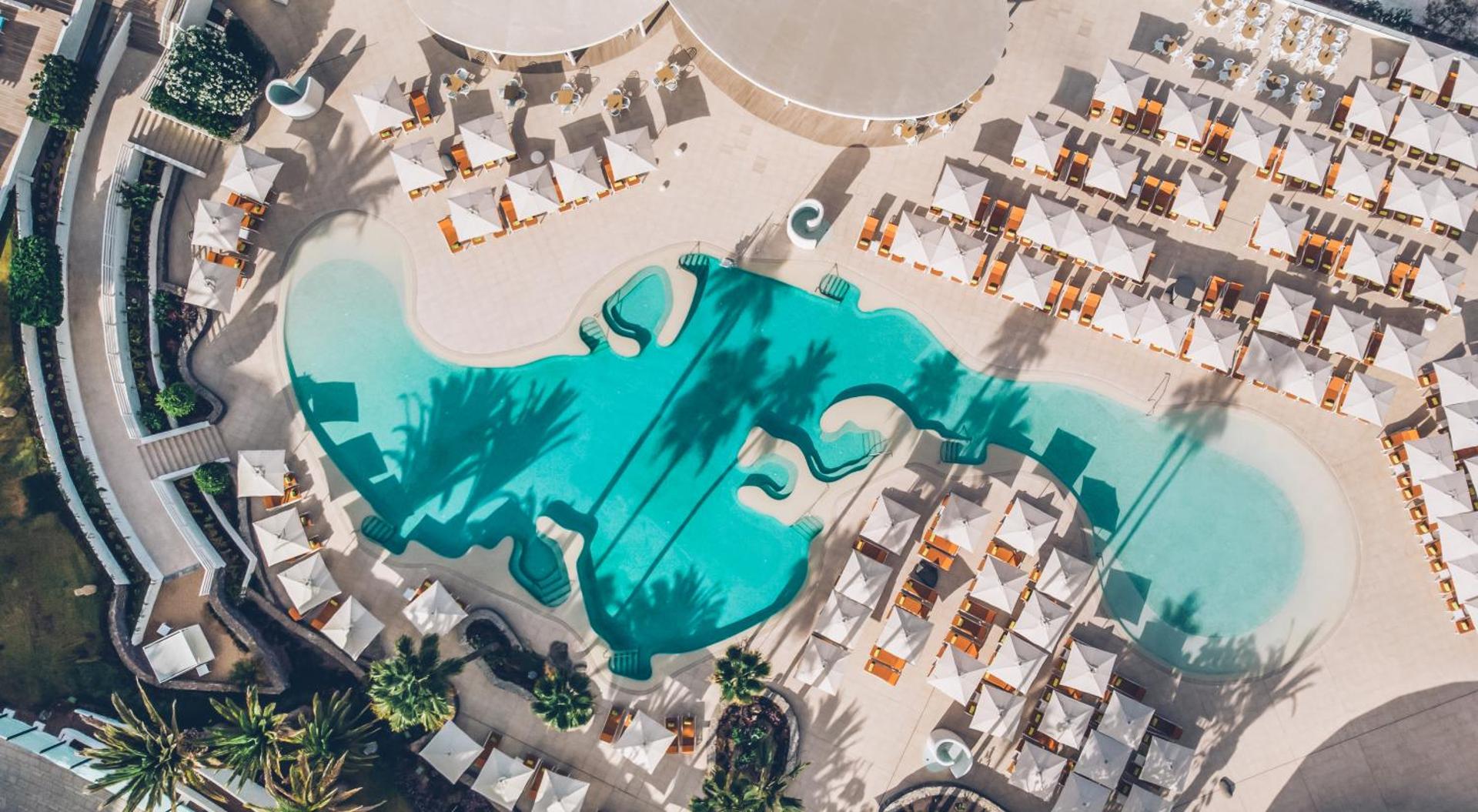 Iberostar Sabila viesnīcas baseina zonas skats no putna lidojuma ar saulessargiem un palmu ēnām Tenerifē