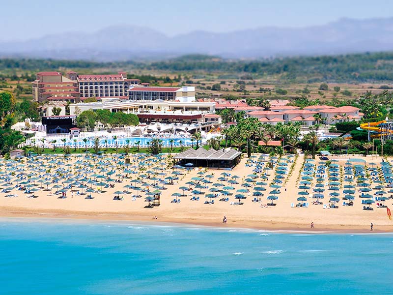 Paloma Oceana viesnīcas panorāmas skats ar plašu smilšu pludmali, ziliem saulessargiem, baseiniem un ēku kompleksu Sidē, Turcijā