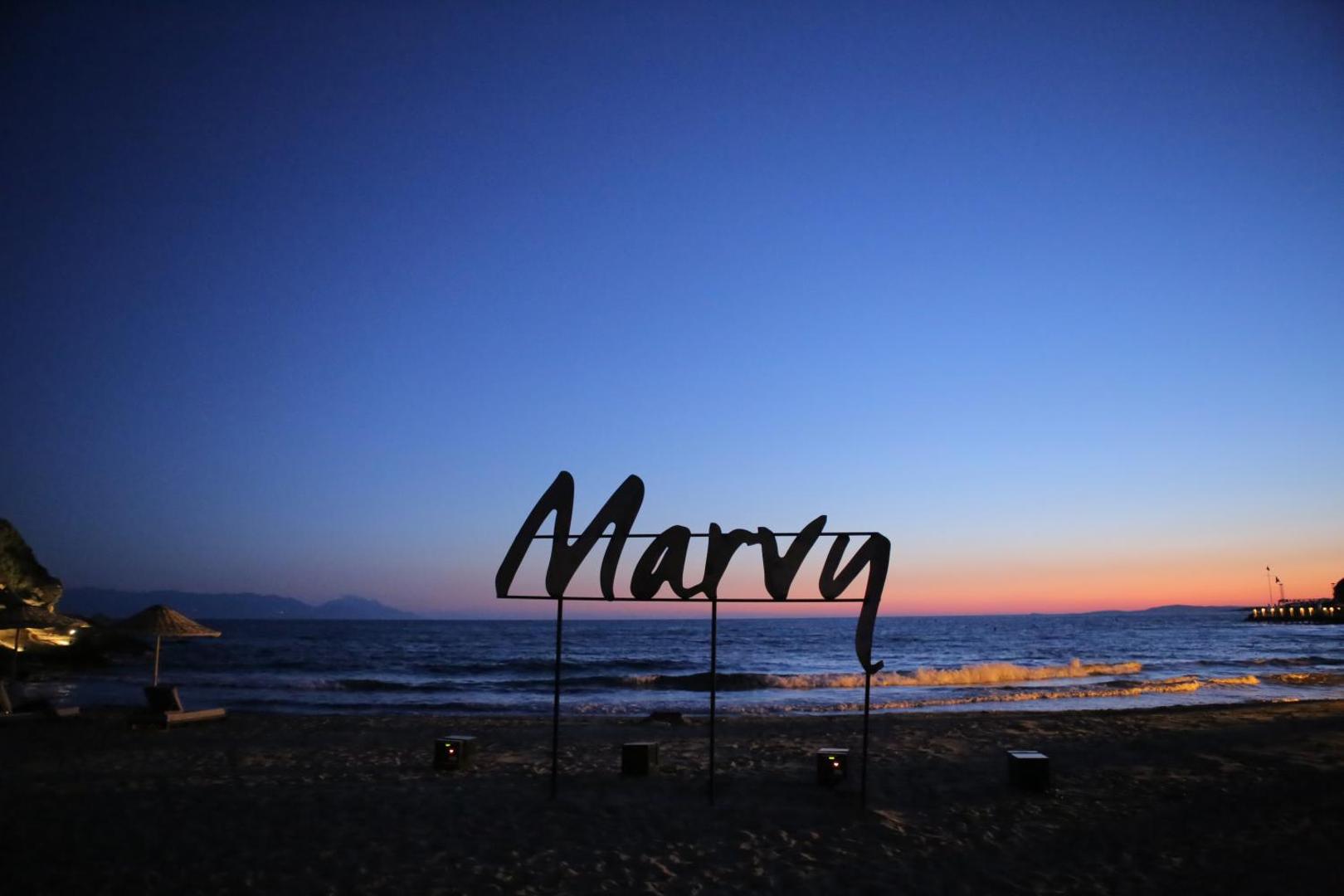 Club Marvy viesnīcas logo zīme smilšainā pludmalē vakarā uz jūras un saulrieta debesu fona Izmiras piekrastē