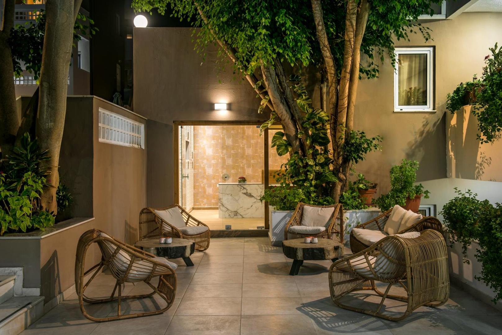 Troulis Apart-Hotel mājīgais āra pagalms vakarā ar pītiem atpūtas krēsliem, koka galdiņiem un zaļojošiem kokiem Bali, Krētā