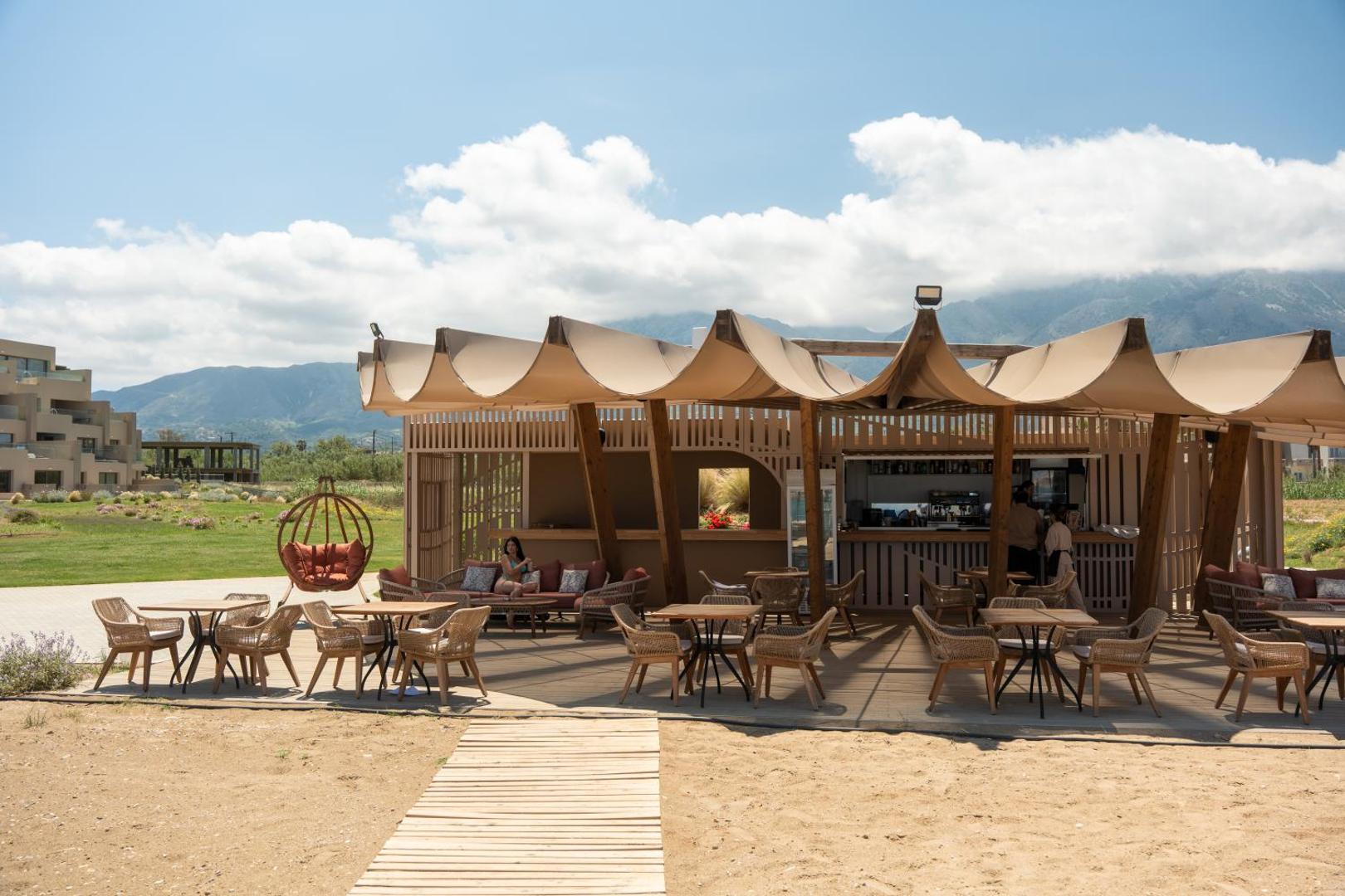 Ventale Island Breeze Resort pludmales bārs un atpūtas zona ar pītiem krēsliem, koka detaļām un skatu uz kalniem fonā
