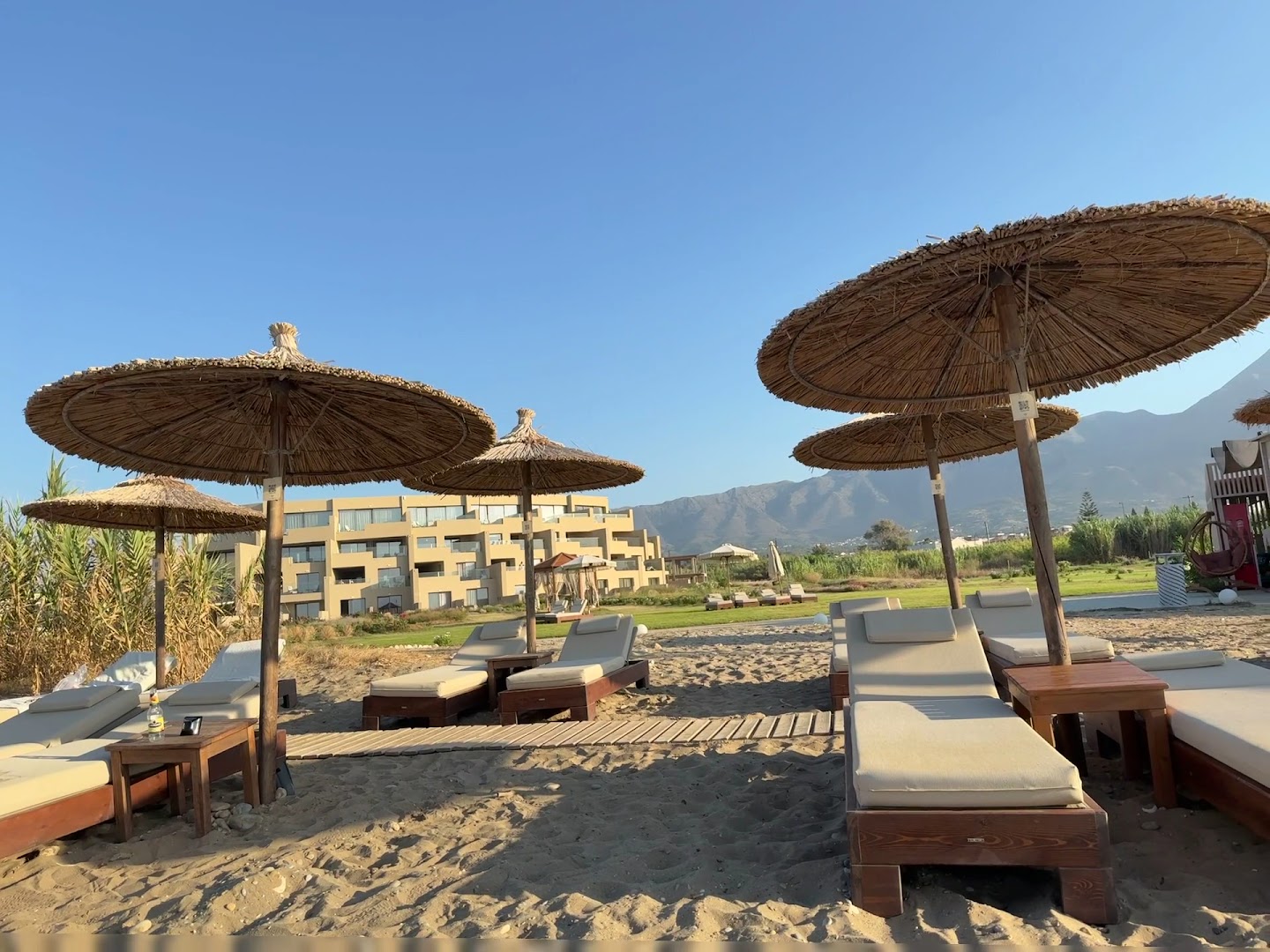 Ventale Island Breeze Resort pludmales zona ar koka sauļošanās krēsliem, salmu saulessargiem un skatu uz viesnīcas korpusu