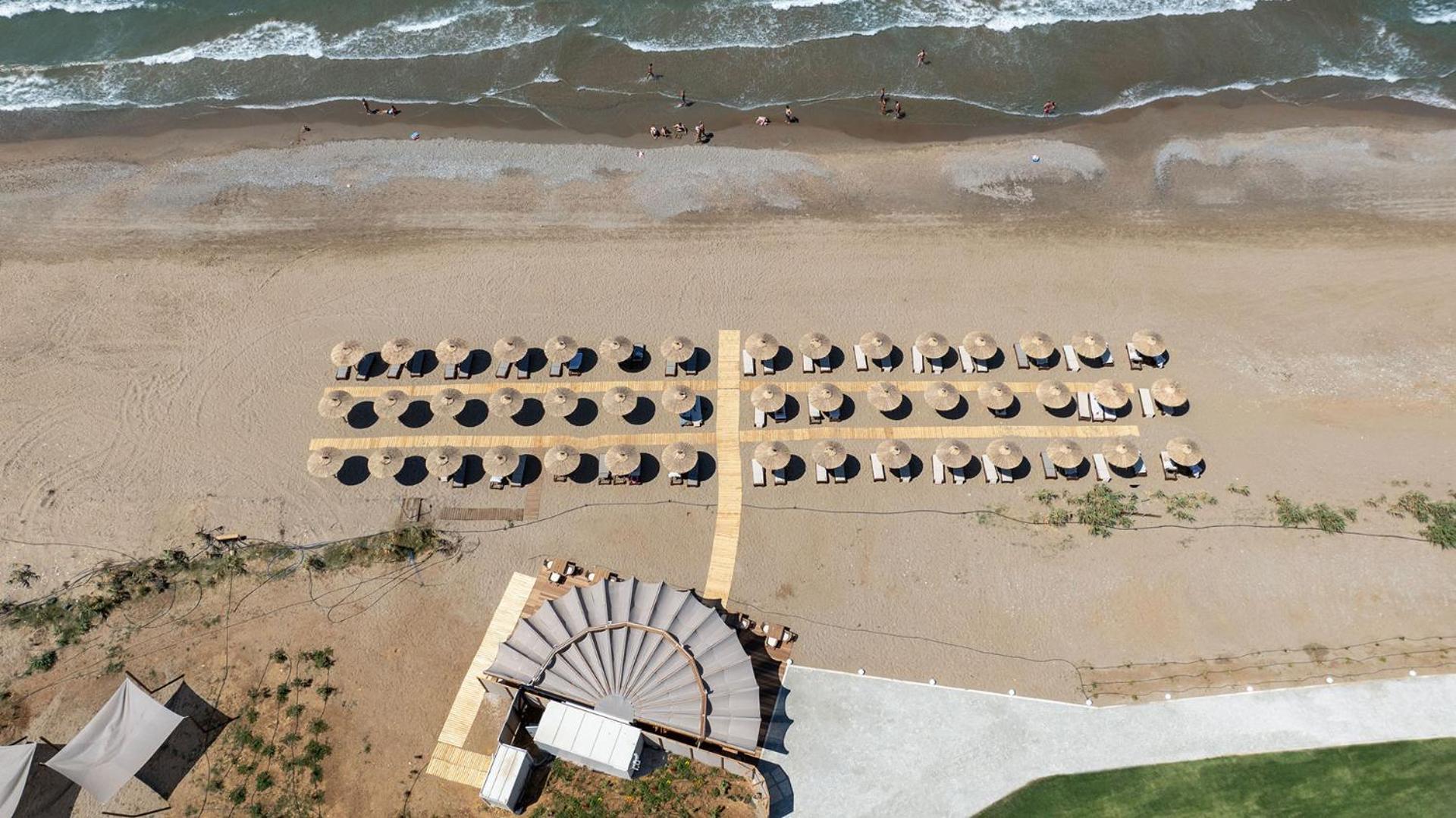 Aerofoto skats uz Ventale Island Breeze Resort privāto pludmali ar saulessargiem, koka laipām un pludmales bāra jumta konstrukciju