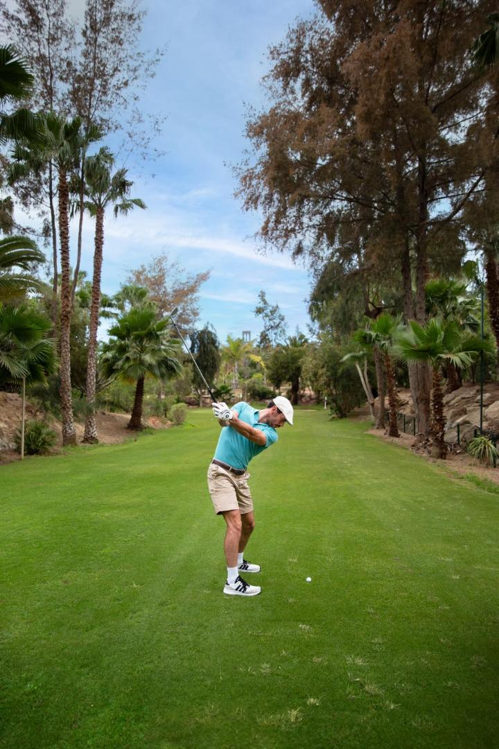 Vīrietis spēlē golfu Bahia del Duque kūrorta zaļajā zonā Tenerifē — apkārtnē palmas un lekni tropu koki