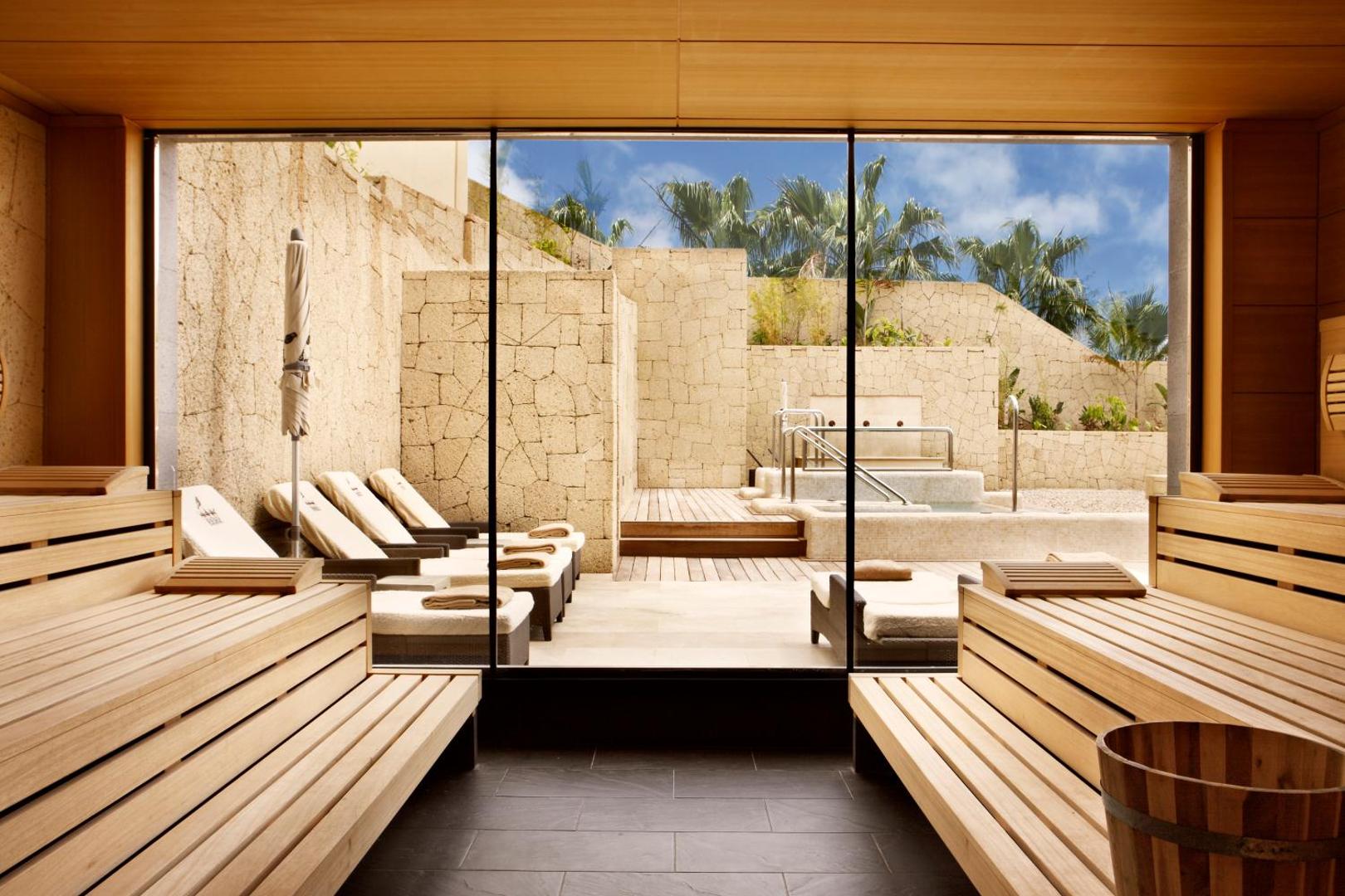 Bahia del Duque spa centra sauna ar koka soliem un skatu caur stikla sienu uz āra atpūtas zonu Tenerifē