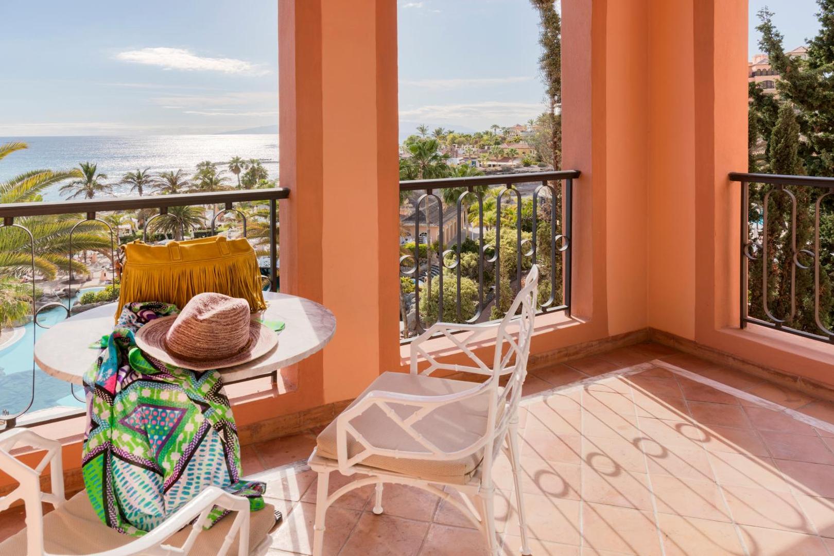 Bahia del Duque viesnīcas balkons ar skatu uz okeānu un palmām Tenerifē, uz galda cepure un soma