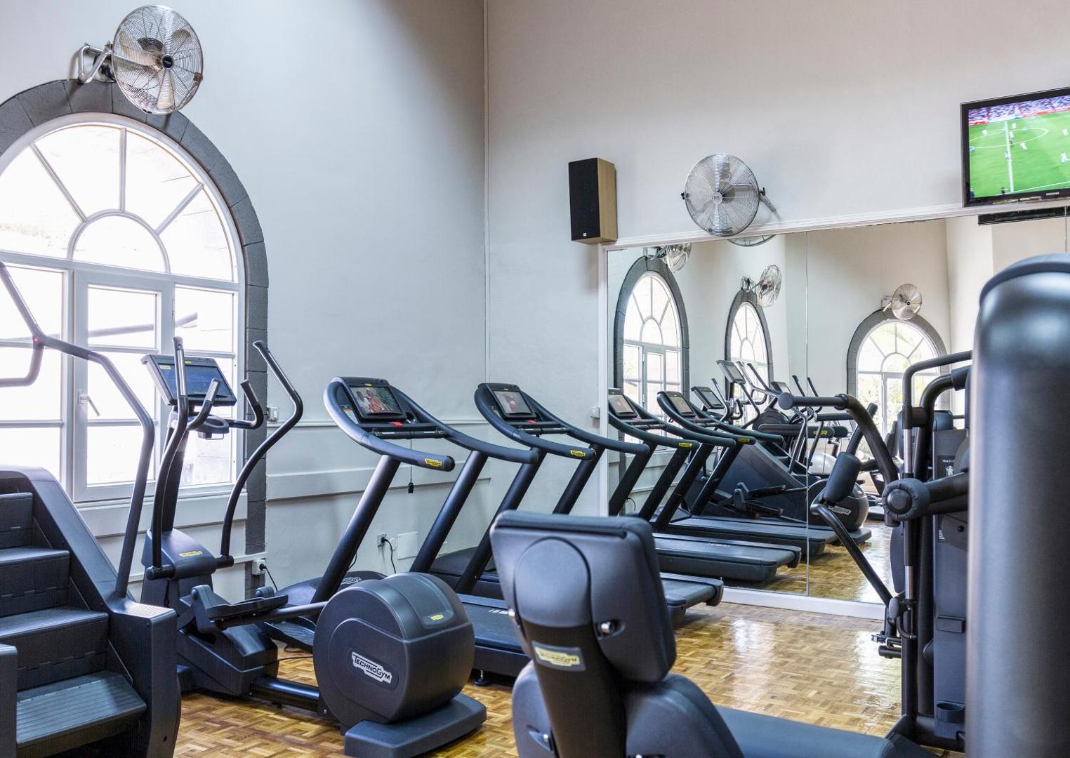 Bahia del Duque sporta zāle ar Technogym skrejceliņiem un kardio trenažieriem — gaiša telpa ar lieliem logiem un ventilatoriem