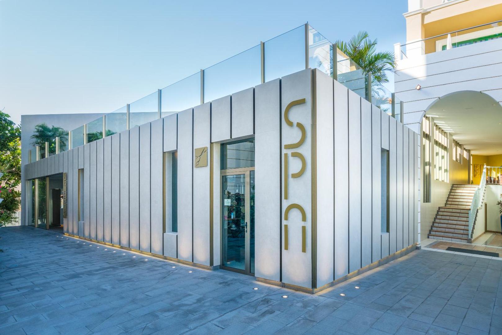 Viesnīcas Jardines de Nivaria modernā spa centra ieeja Tenerifē — gaiša fasāde ar stikla elementiem un akmens flīžu klājumu.