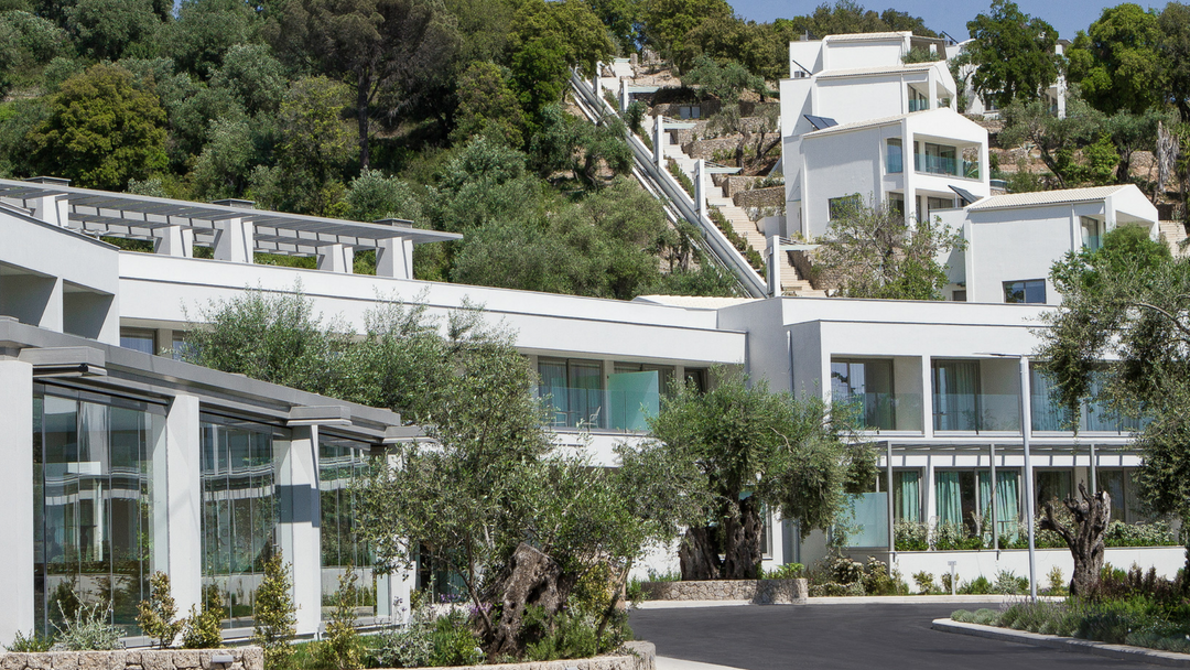 Rodostamo Hotel & Spa galvenā ēka un villas kalna nogāzē ar funikulieri — mūsdienīga arhitektūra Korfu ainavā